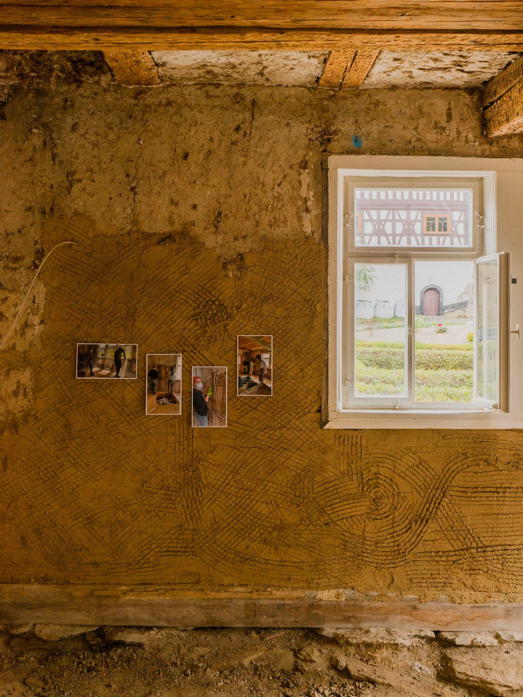 Frisch lehmverputzte Wand mit Fenster und angehefteten Fotos