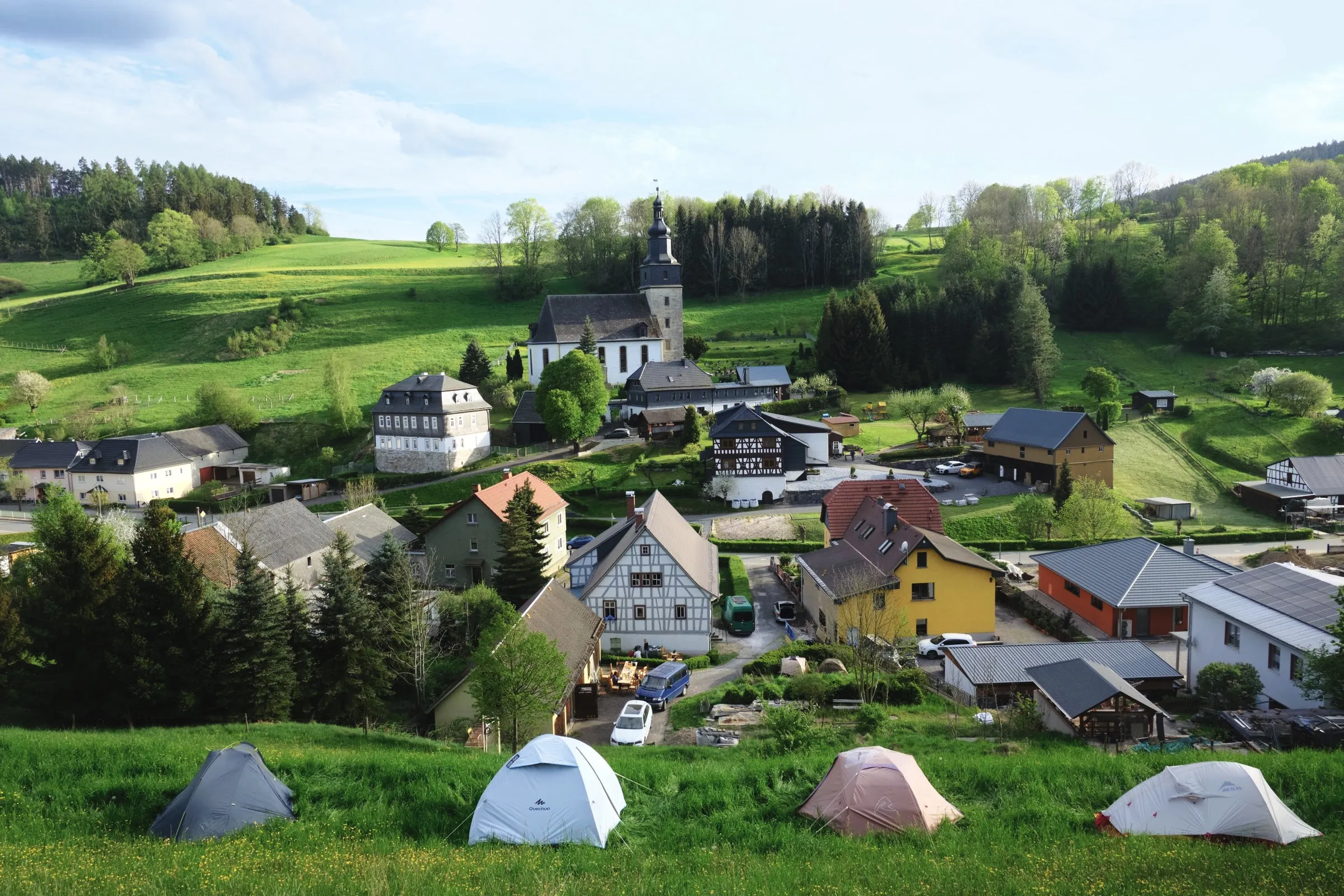 Zelte auf einer Wiese oberhalb von Döschnitz, im Tal das Dorf mit Kirche
